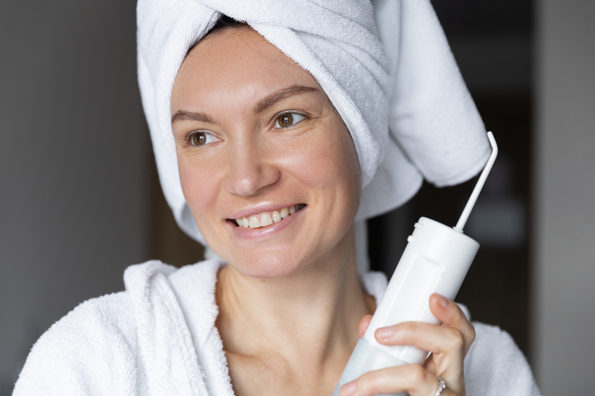 Smiling woman holding a cordless water flosser as part of her oral hygiene routine.