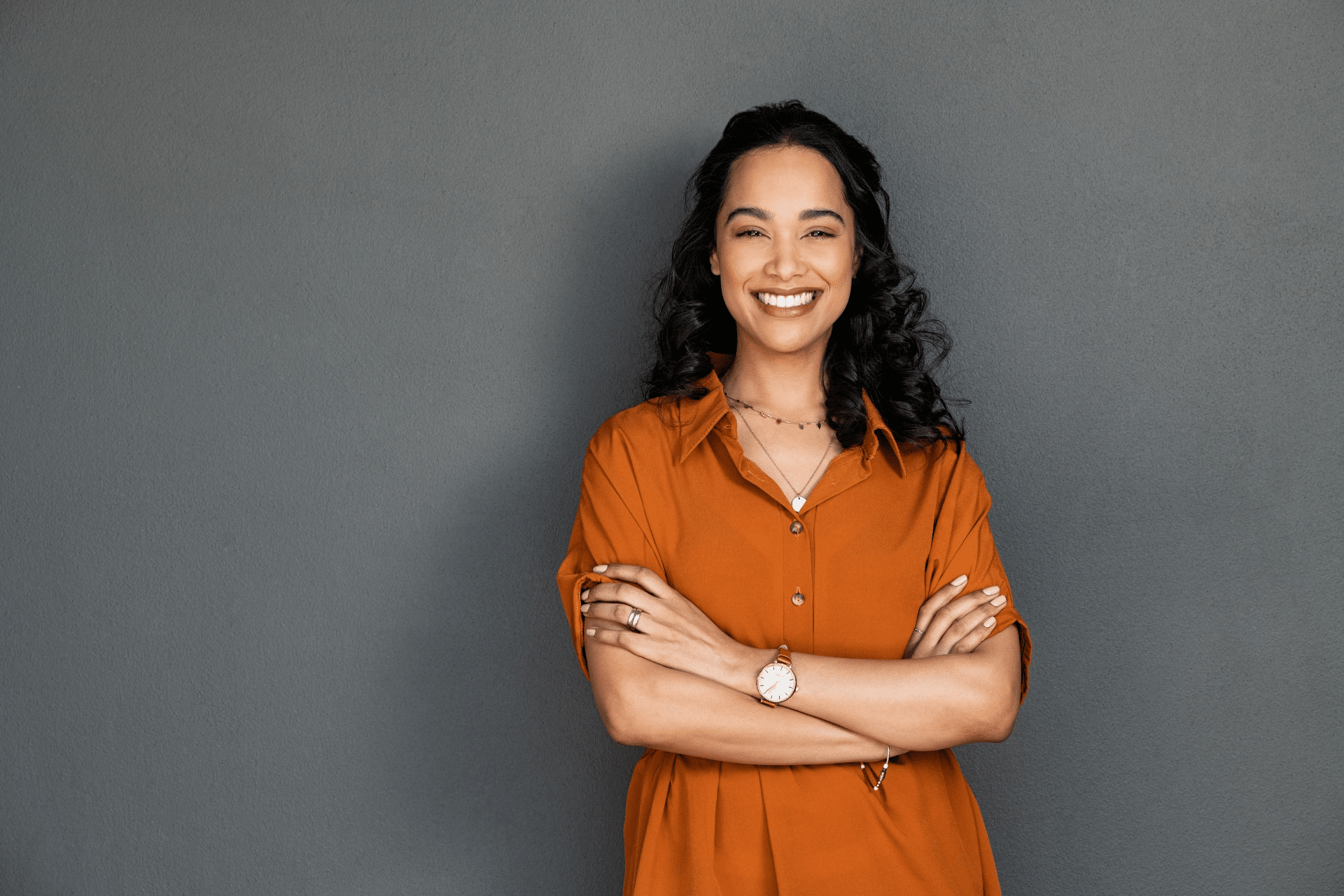 Smiling woman standing with her arms crossed against a gray background