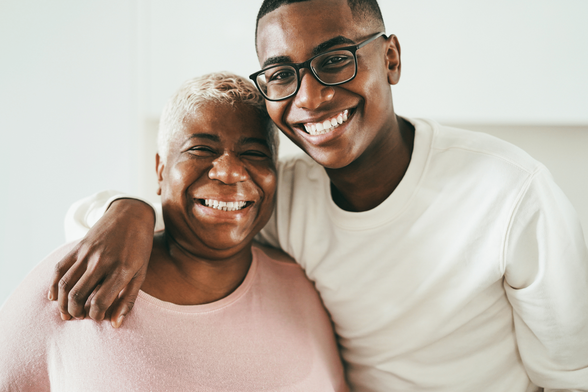 Young man and senior woman smiling brightly while hugging indoors.